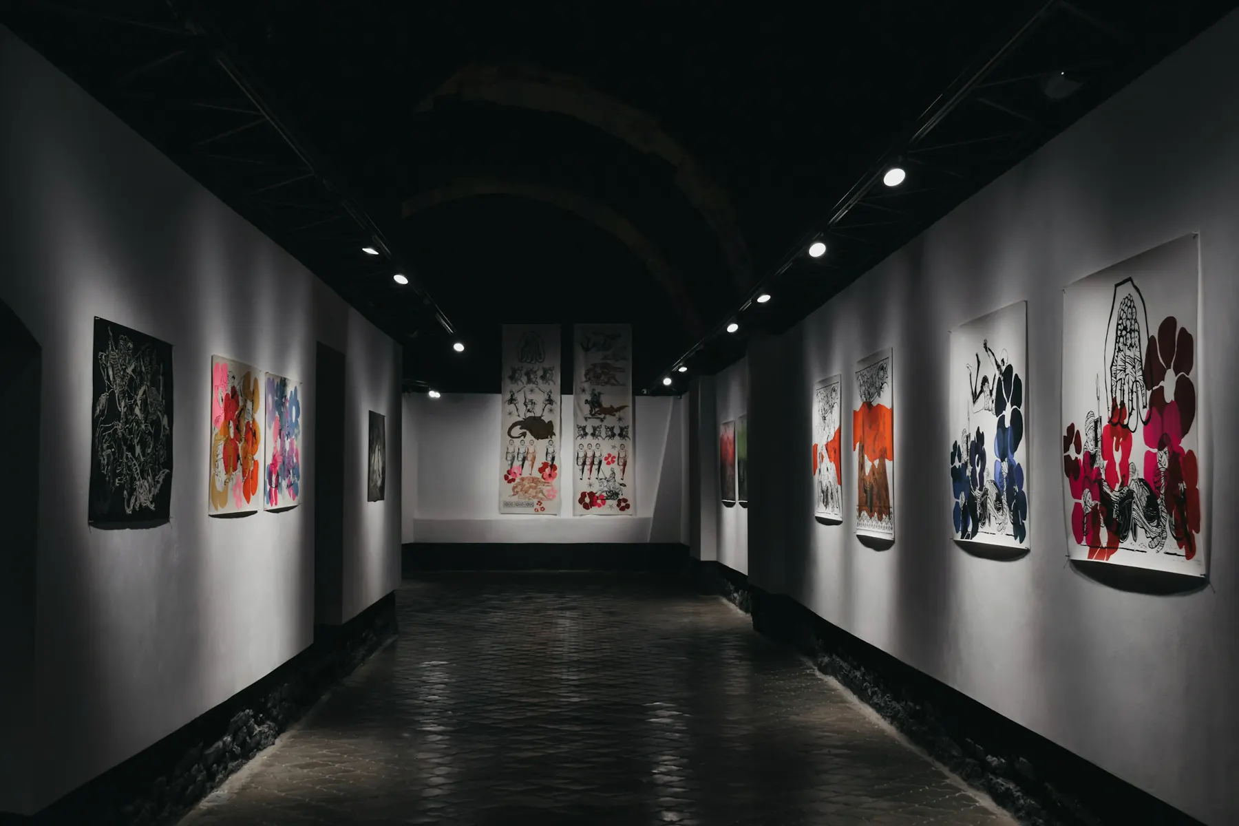A long, dim gallery hall with large paintings hung far apart on pale walls