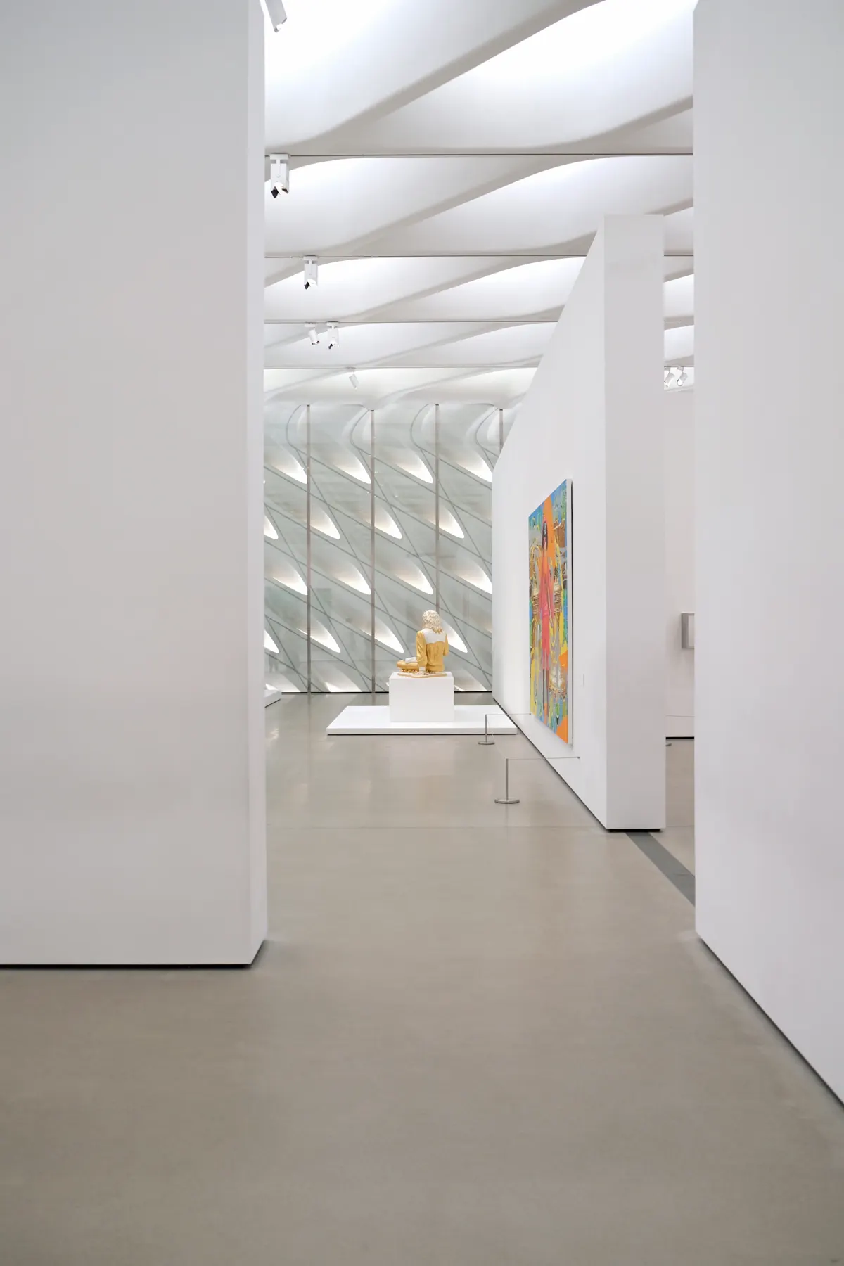A bright, empty gallery: white walls, pale floor and a single sculpture at the end of the room